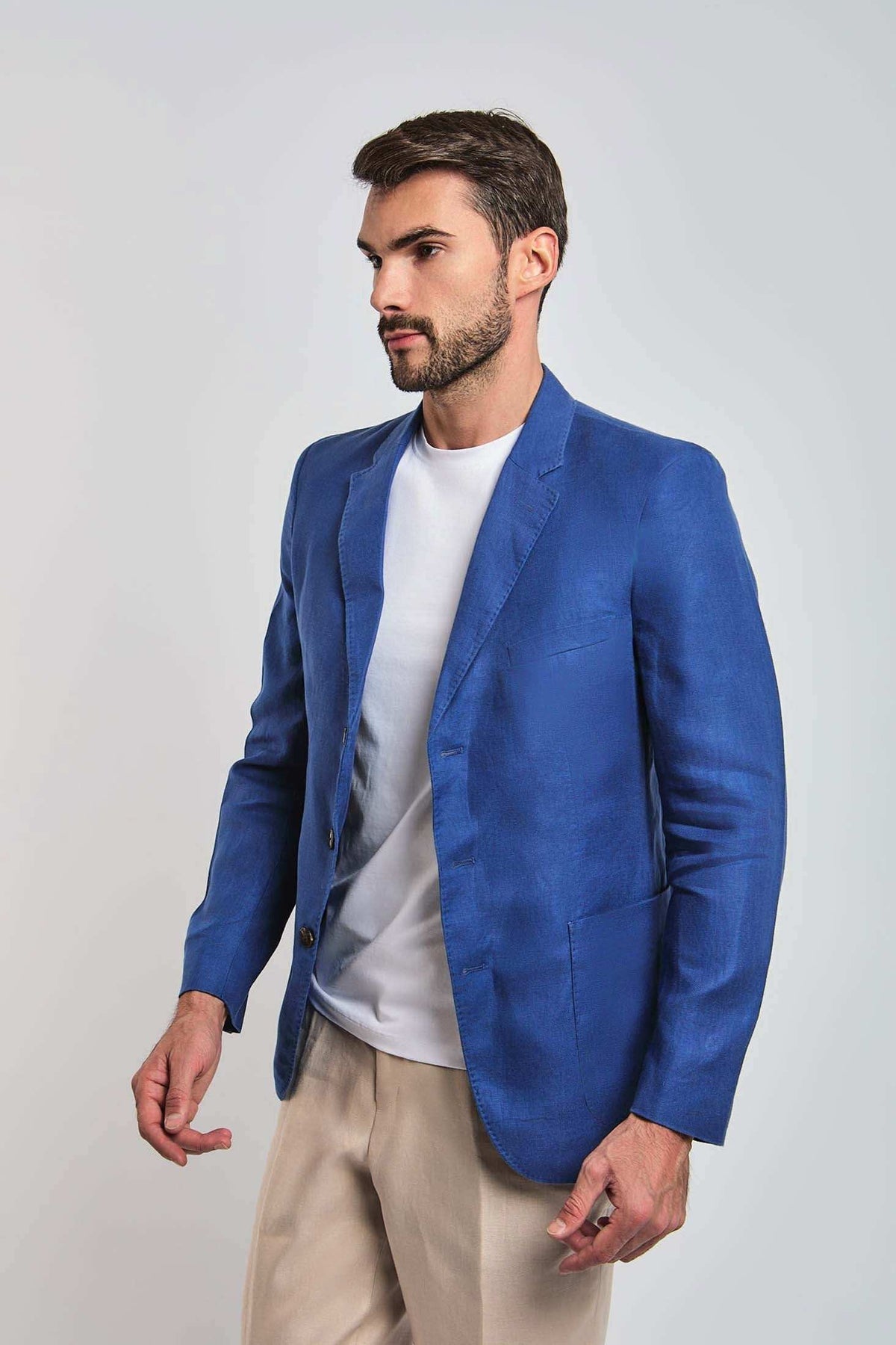 Man wearing a blue blazer, white t-shirt, and beige pants on a plain background
