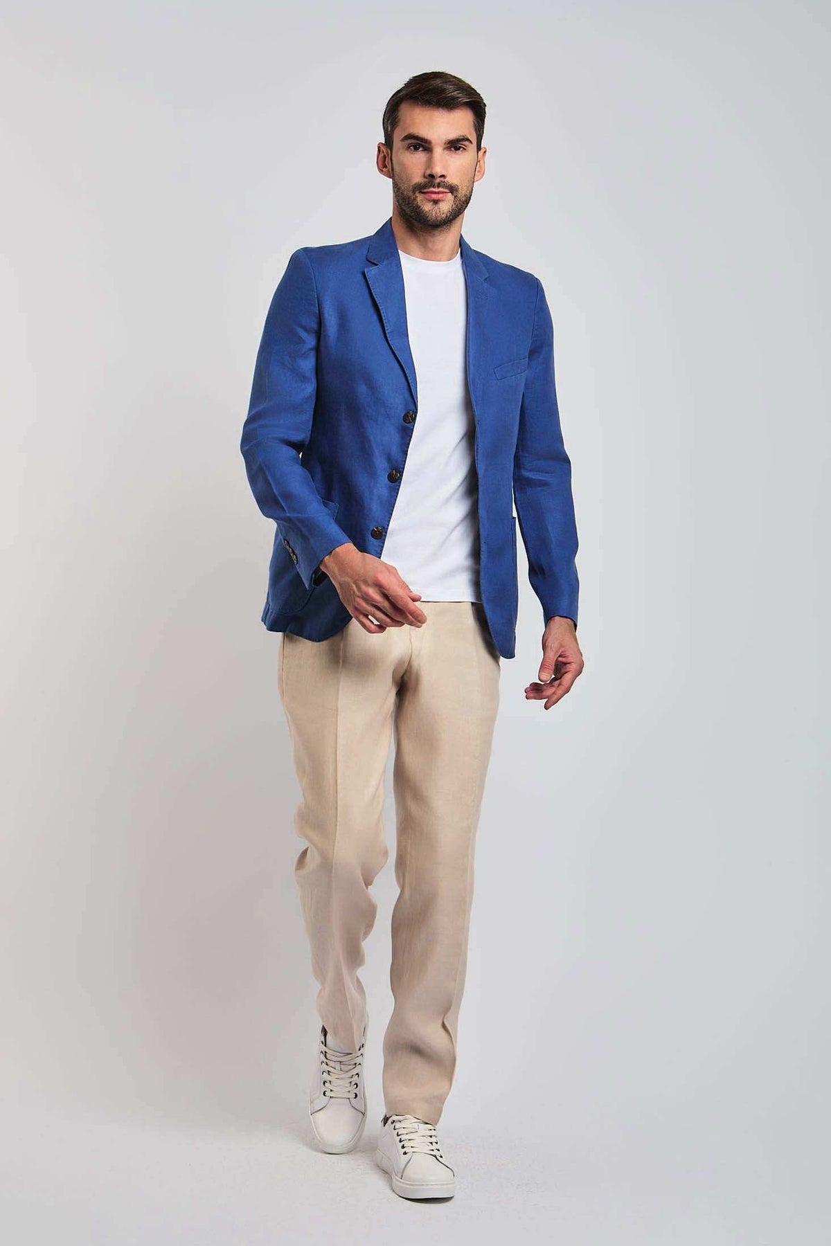 Man in a blue blazer, white t-shirt, beige pants, and white sneakers on light background
