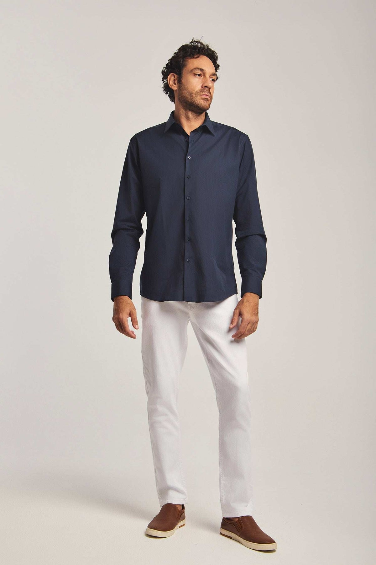 Dalydress men's fashion model in navy shirt, white pants, and brown shoes, studio background