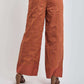Back view of woman wearing wide leg rust orange embroidered pants with eyelet details