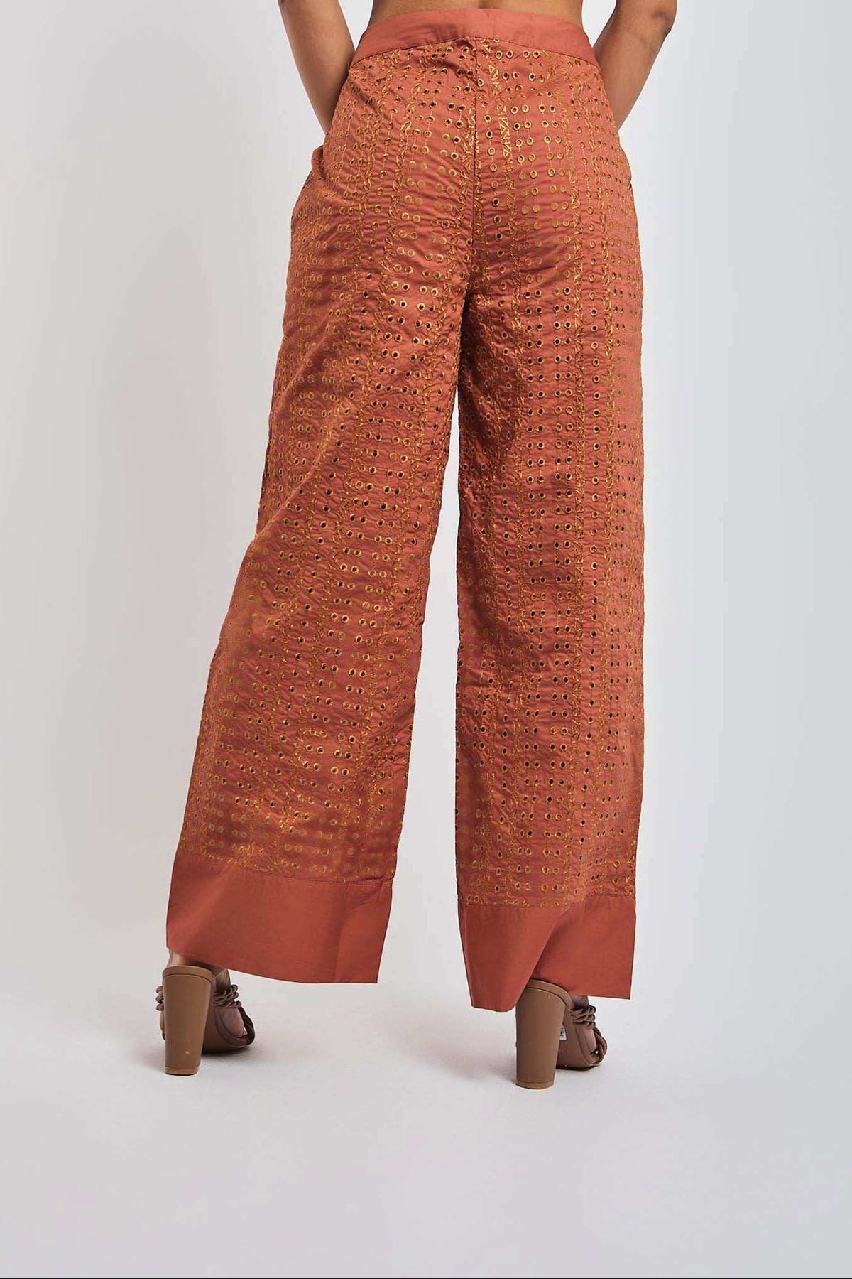 Back view of woman wearing wide leg rust orange embroidered pants with eyelet details
