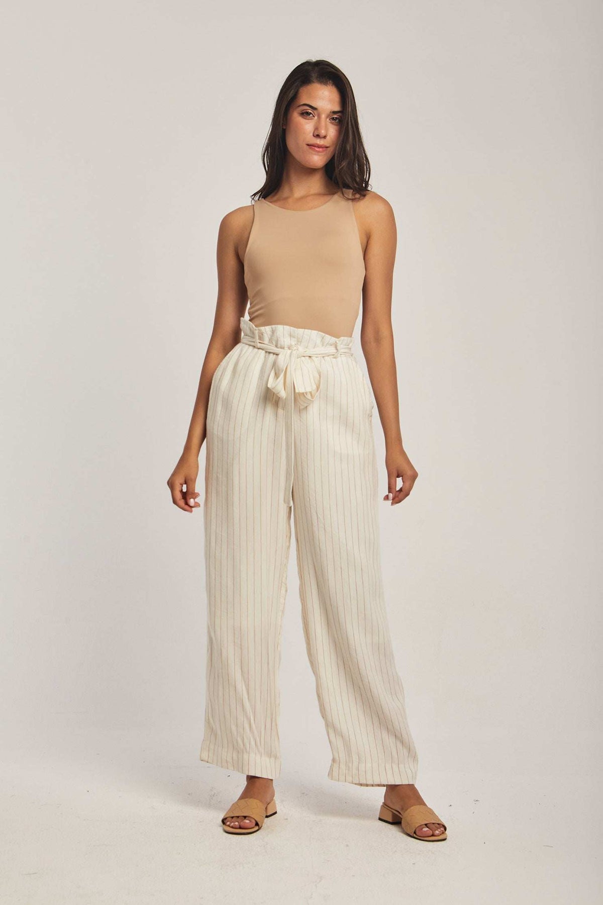 Woman wearing Dalydress beige sleeveless top and striped high-waisted pants, studio setting
