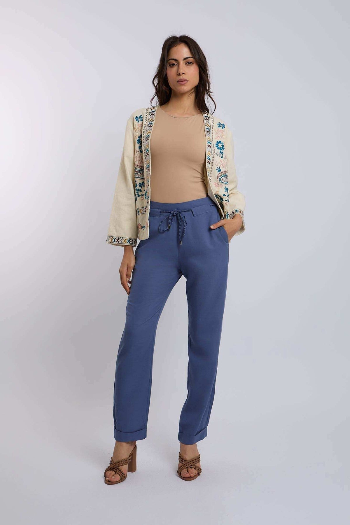 Woman wearing beige top, embroidered cream jacket, blue pants, and heels, Dalydress fashion.