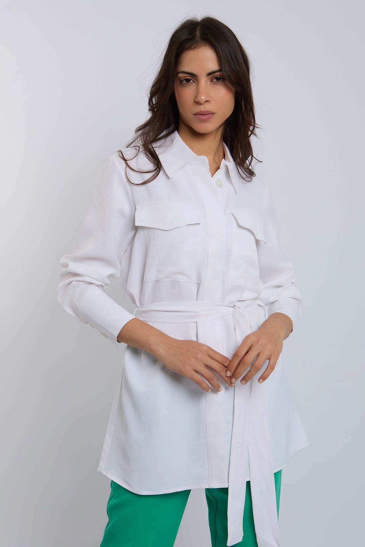 Woman modeling Dalydress white belted shirt with flap pockets and green pants, studio background