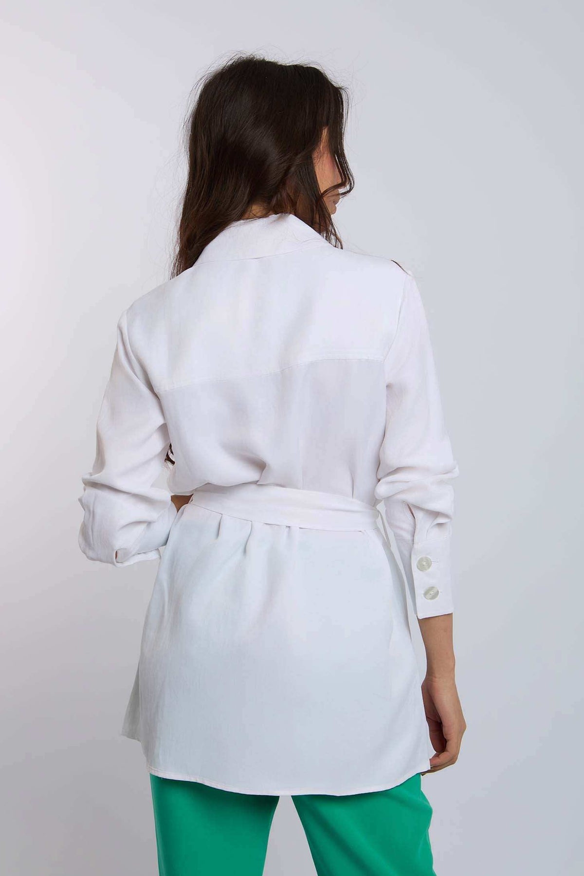 Woman modeling Dalydress white belted shirt with button cuffs and green pants, back view
