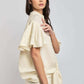 Woman wearing cream short sleeve blouse with ruffled sleeves and matching pants