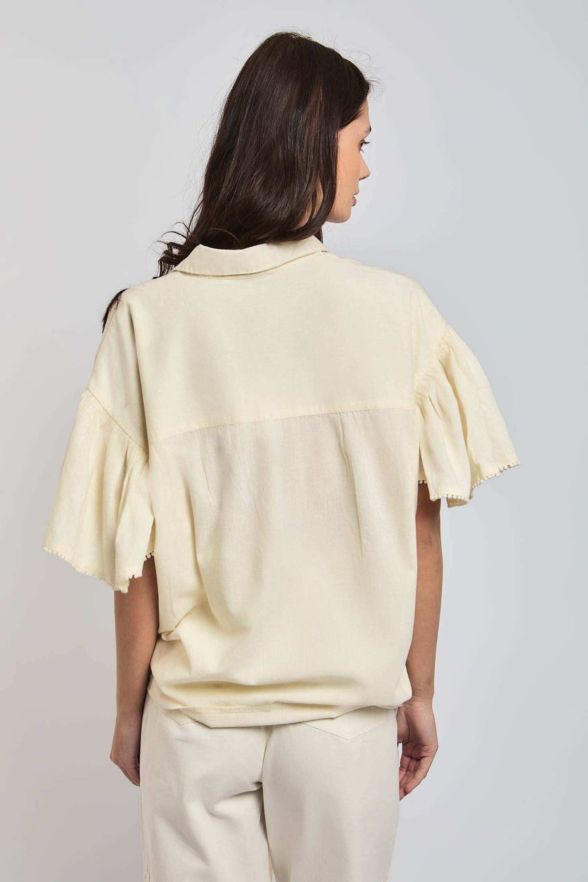 Woman wearing loose beige short sleeve blouse and matching pants, facing backwards