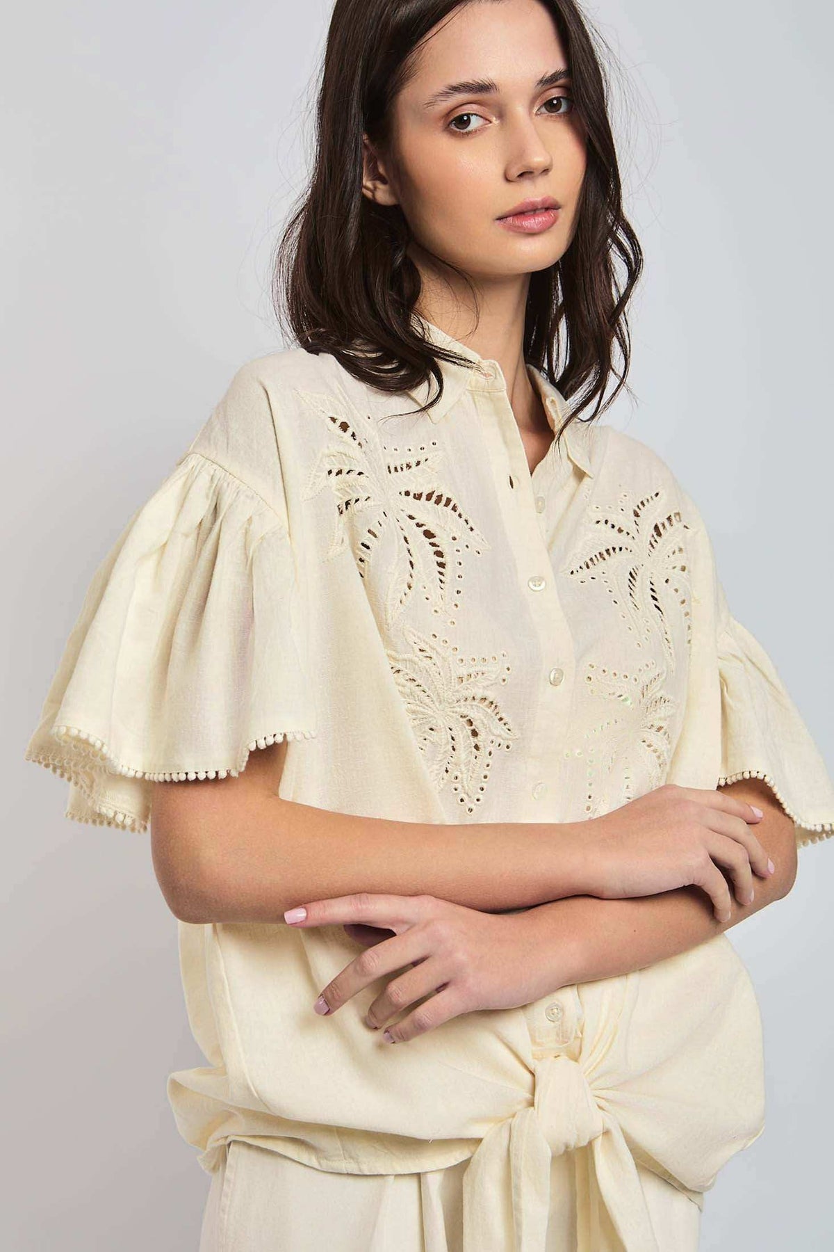 Woman wearing a cream short-sleeve embroidered blouse with eyelet details and tie front