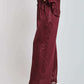 Woman wearing burgundy wide-leg satin pants and matching top with nude heels