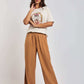 Woman modeling white graphic t-shirt and wide-leg light brown pants against plain background