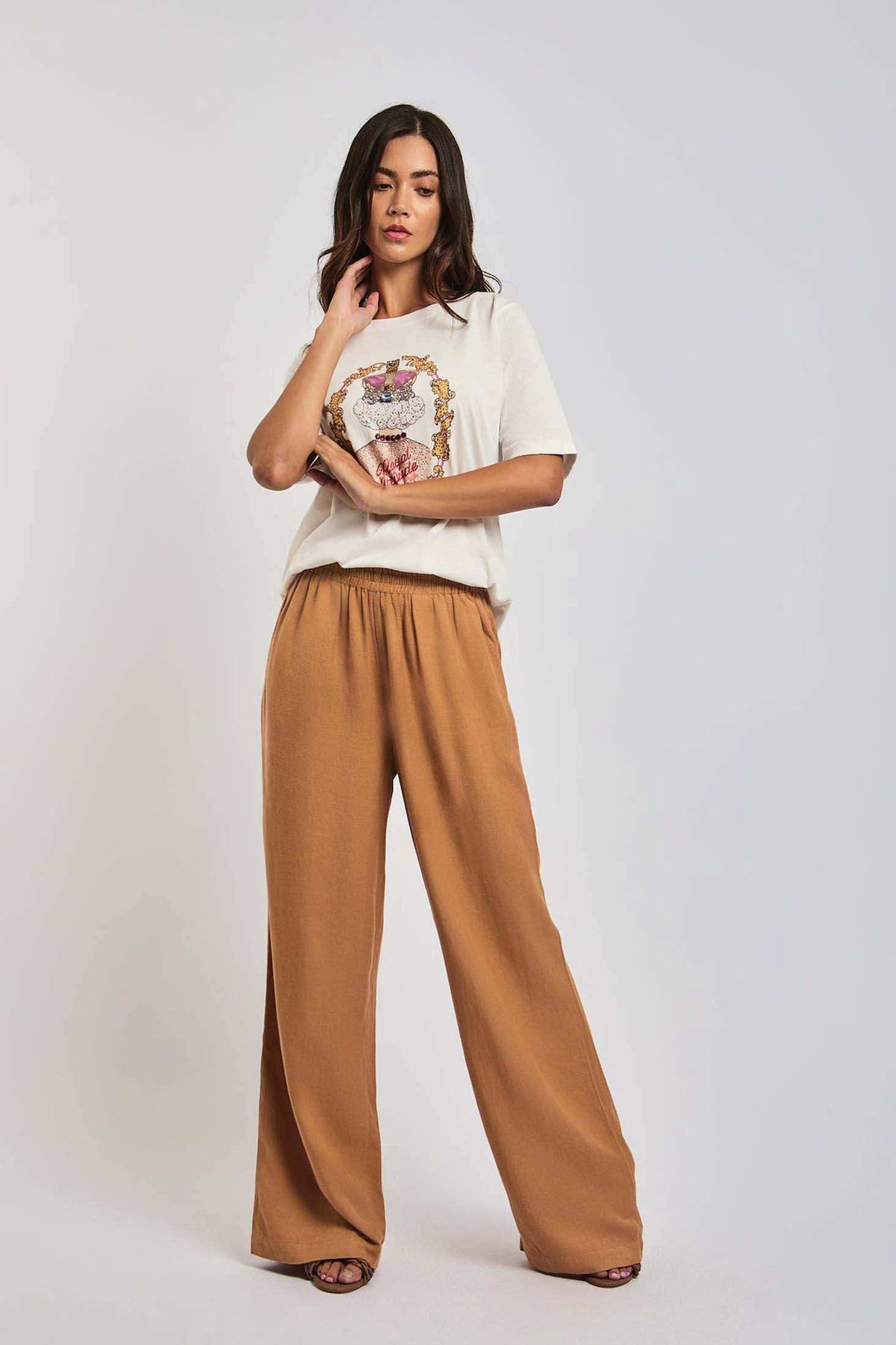 Woman modeling white graphic t-shirt and wide-leg light brown pants against plain background