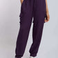 Woman wearing purple cargo pants with side pockets, white sneakers, and a crop top