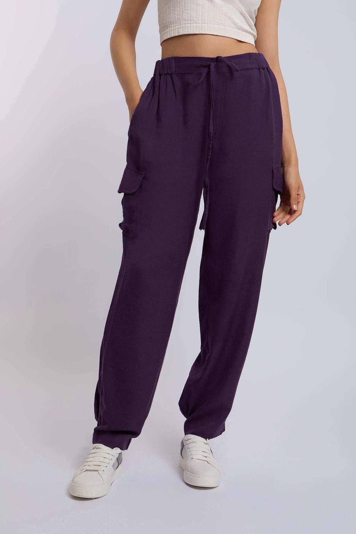 Woman wearing purple cargo pants with side pockets, white sneakers, and a crop top