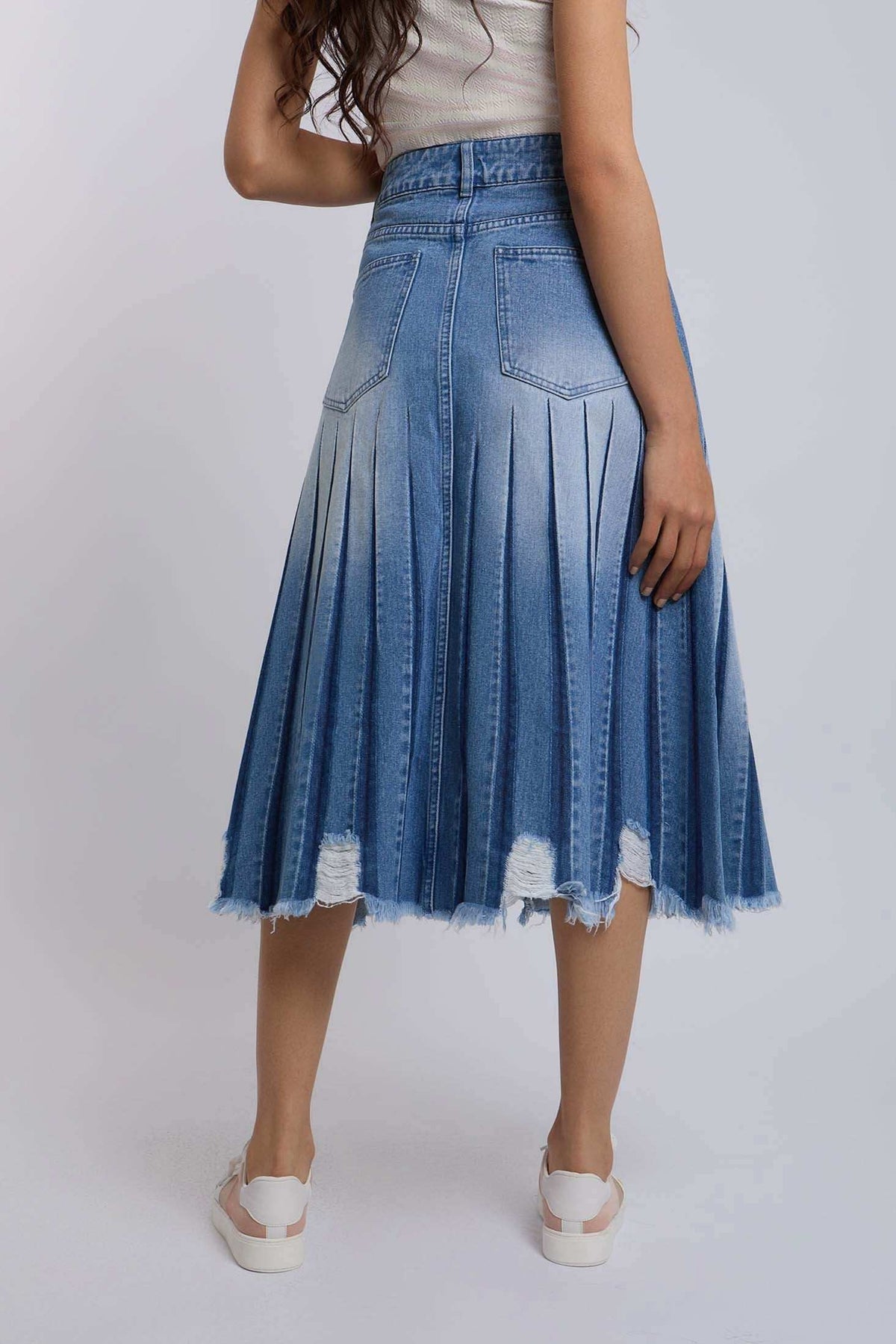 Woman wearing pleated denim midi skirt with frayed hem and white sneakers, back view