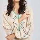 Woman wearing cream peasant dress with colorful floral embroidery and long sleeves