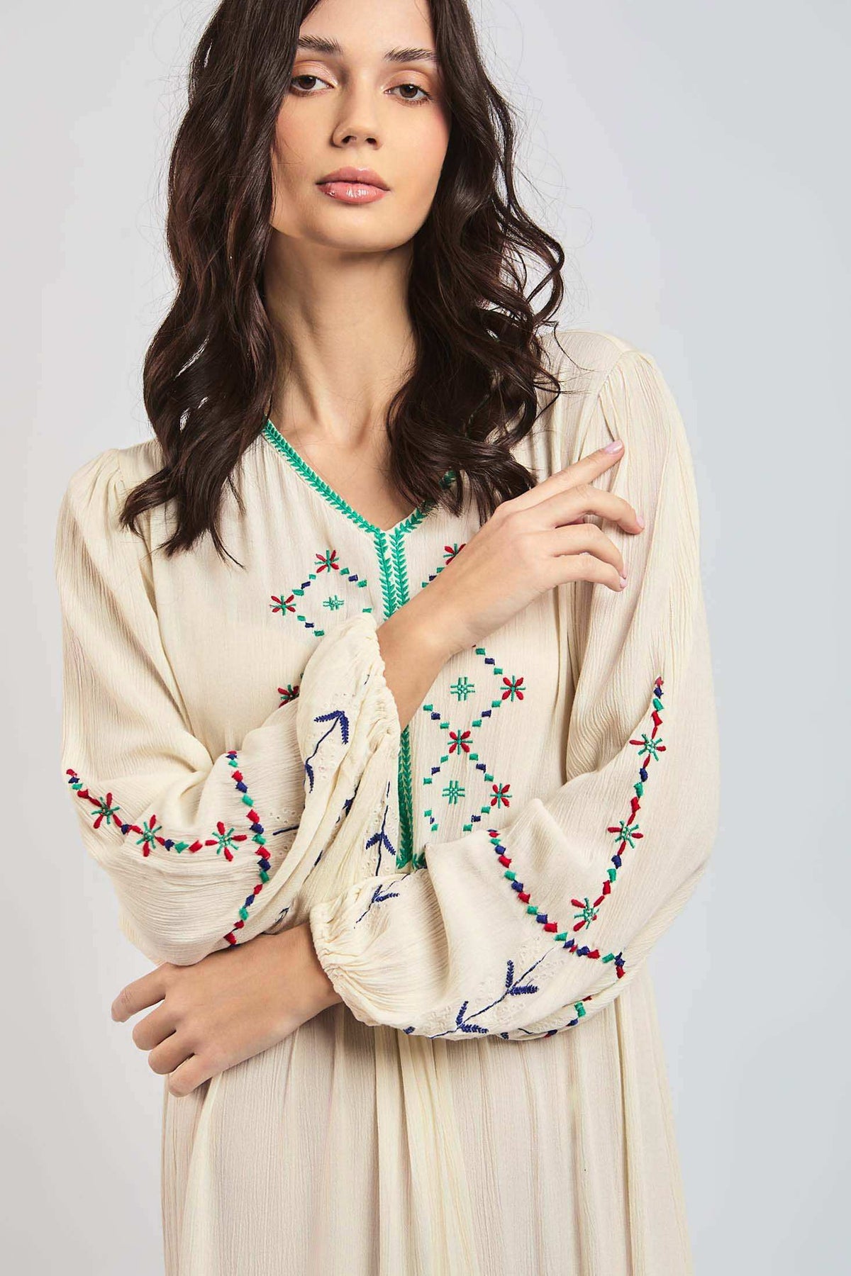 Woman wearing cream peasant dress with colorful floral embroidery and long sleeves