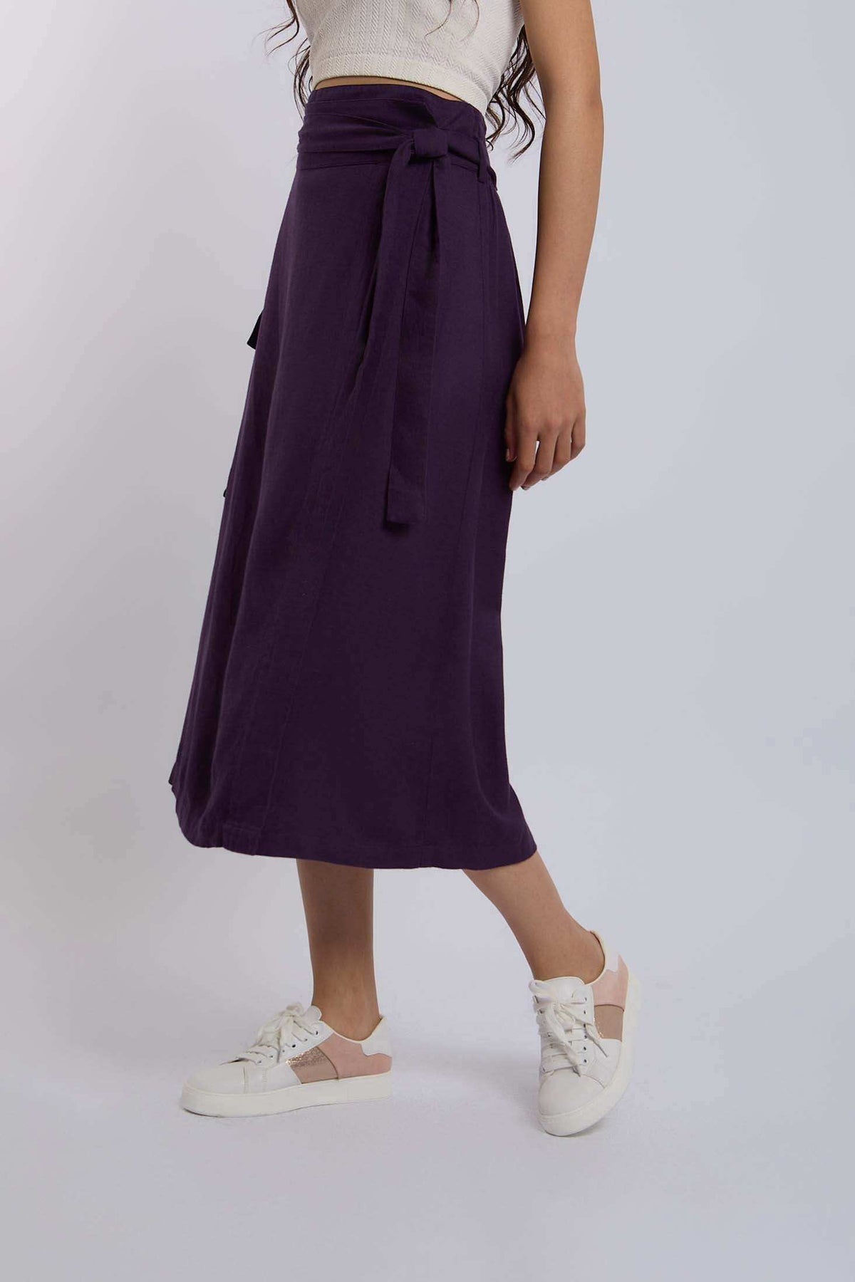 Woman wearing a purple high-waist midi skirt with tie belt and white sneakers