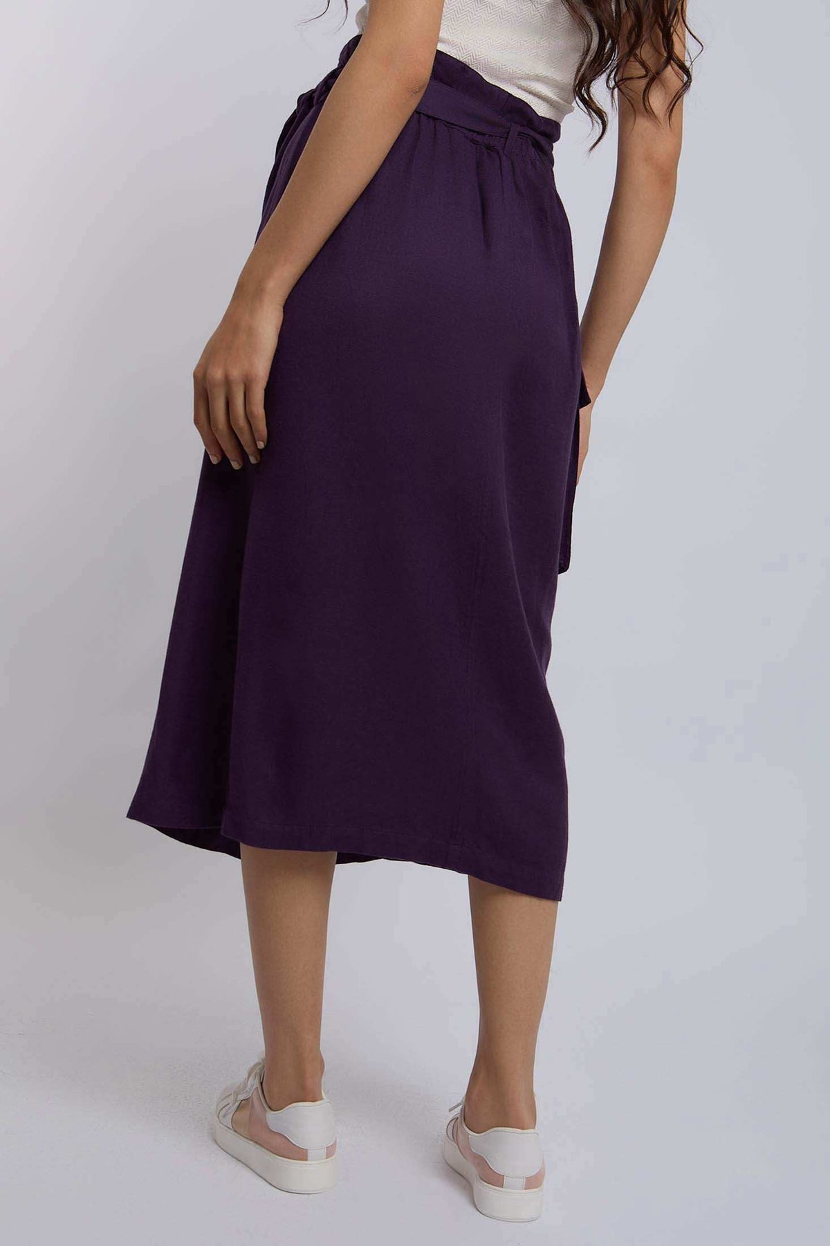 Woman wearing a high-waisted purple midi skirt with white sneakers, back view