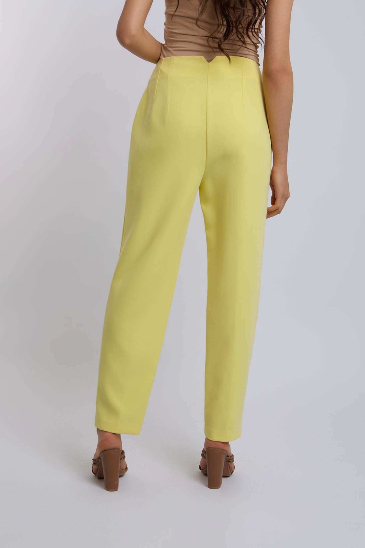 Woman wearing high-waisted yellow pants and brown heels, back view, casual fashion