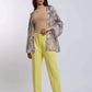 Woman wearing a beige top, yellow trousers, and a colorful paisley open jacket
