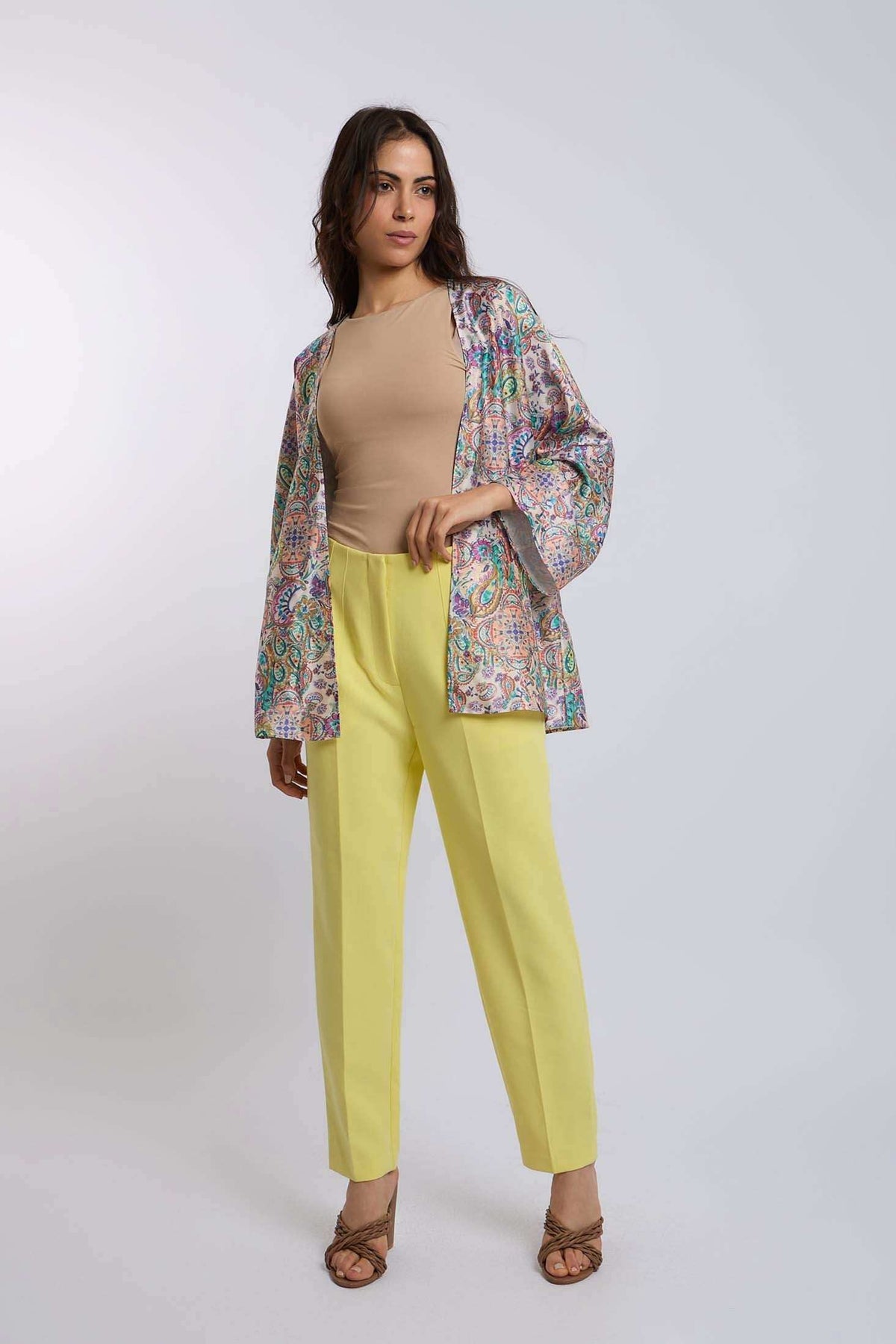 Woman wearing a beige top, yellow trousers, and a colorful paisley open jacket