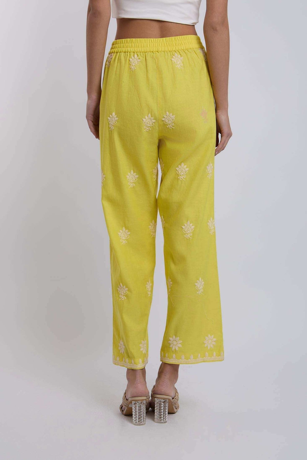 Back view of woman wearing yellow embroidered straight-leg pants, clear block heels