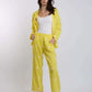 Woman wearing a yellow embroidered pants and jacket set with white tank top, standing in studio