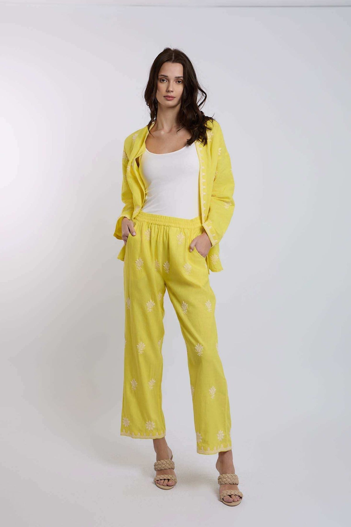Woman wearing a yellow embroidered pants and jacket set with white tank top, standing in studio