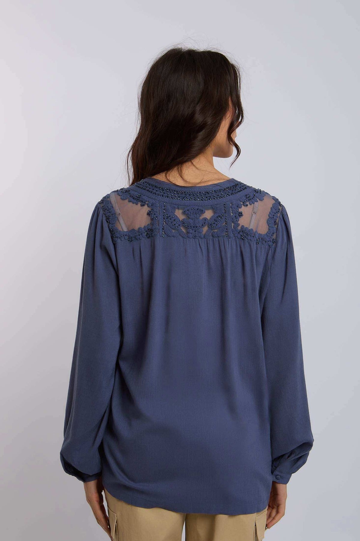 Woman wearing a long sleeve blue blouse with lace and sheer panel details on the back