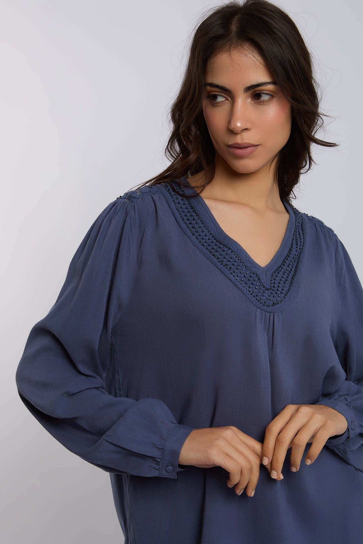 Woman wearing a blue long sleeve blouse with V-neck and textured trim detail