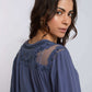 Woman in blue blouse with sheer embroidered yoke and beaded accents, facing sideways