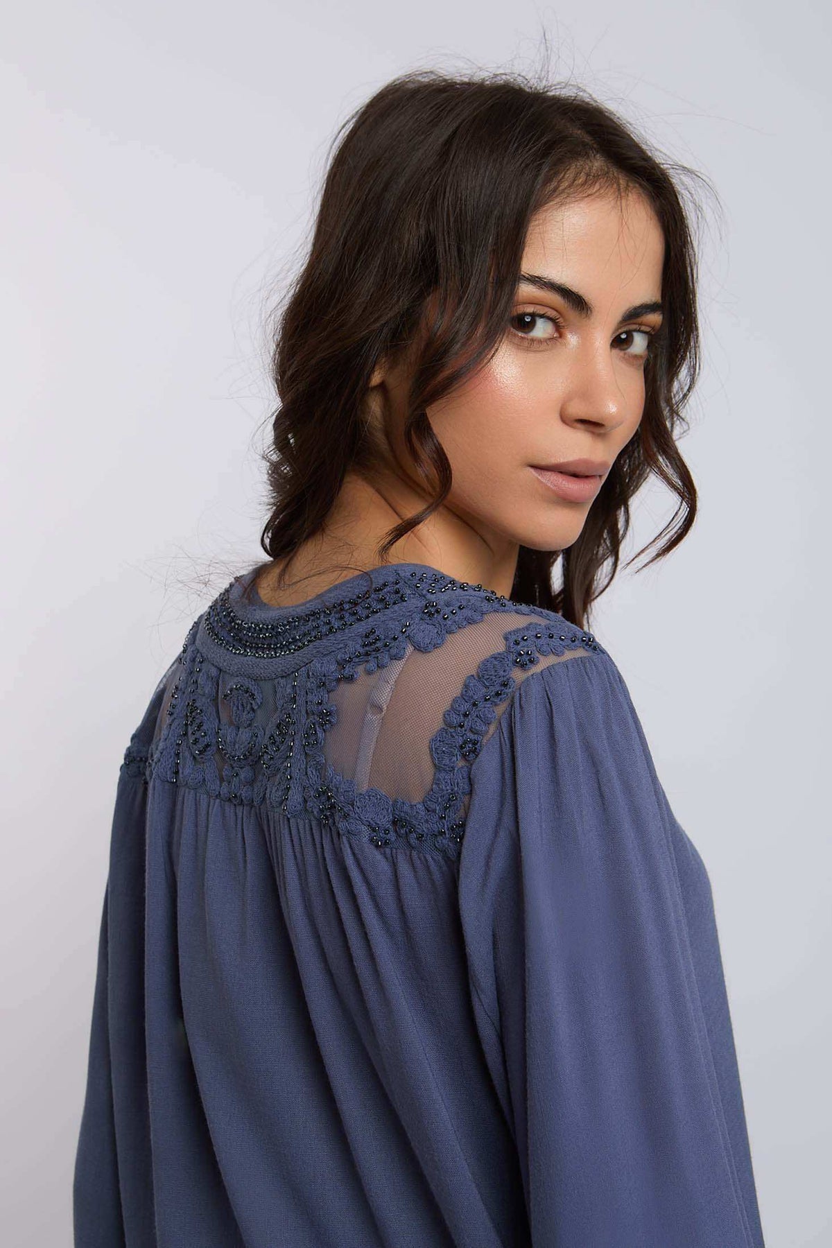 Woman in blue blouse with sheer embroidered yoke and beaded accents, facing sideways