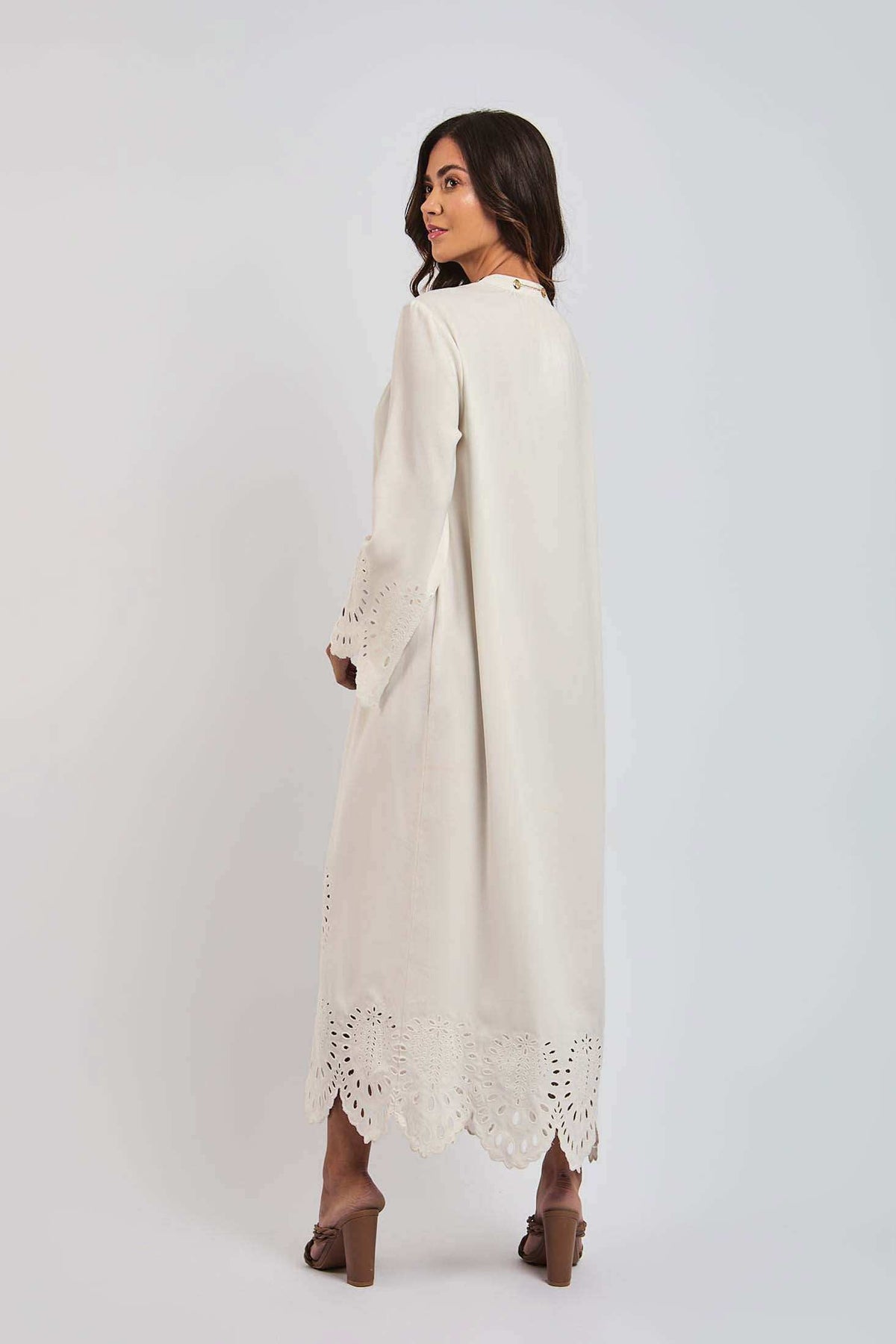 Woman wearing a long cream dress with lace cutout details on sleeves and hem