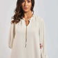 Woman wearing cream long sleeve dress with eyelet sleeves and gold chain detail