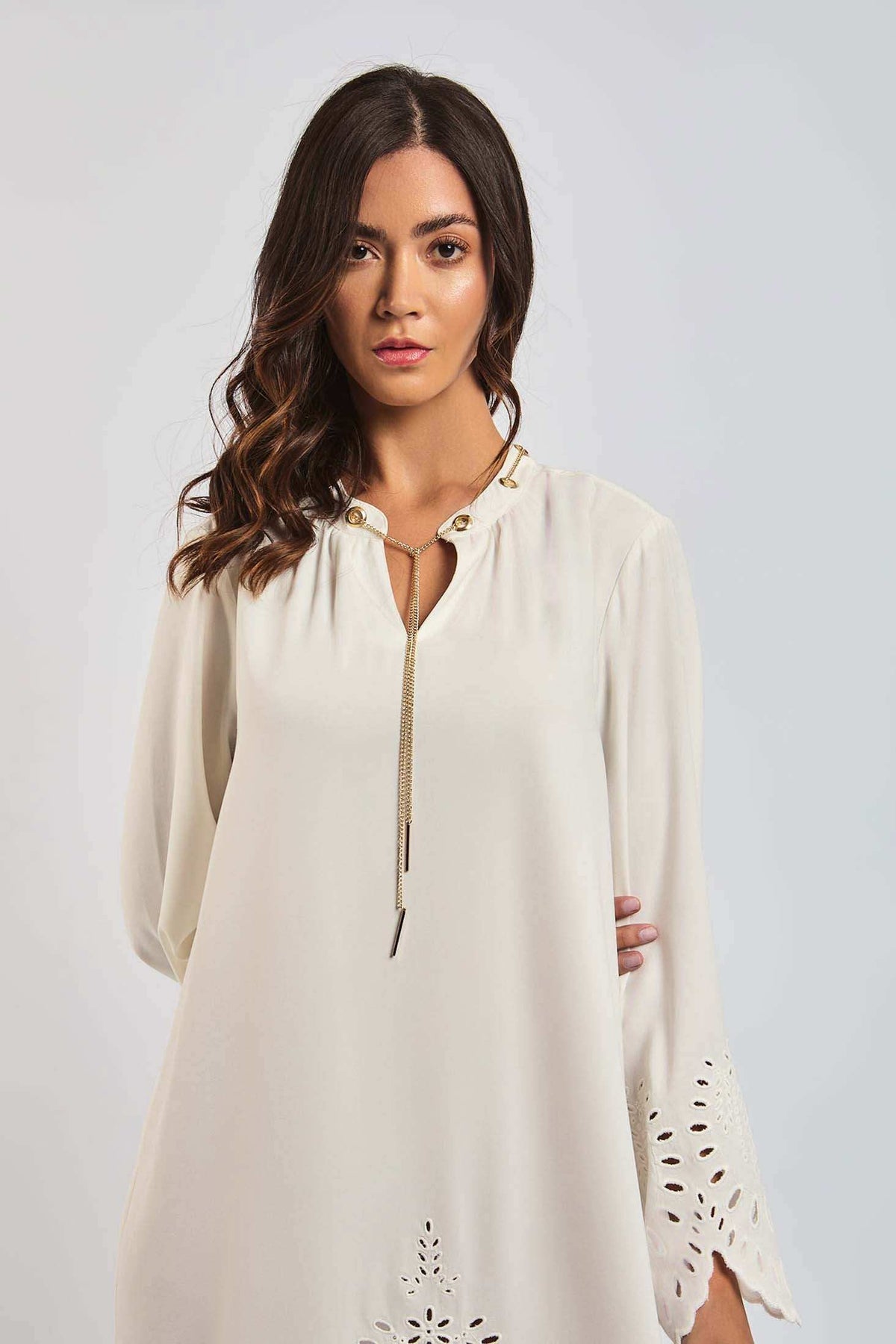 Woman wearing cream long sleeve dress with eyelet sleeves and gold chain detail