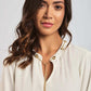 Woman with wavy hair wearing a white blouse with gold button details and chain necklace