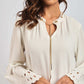 Woman wearing a cream blouse with eyelet lace bell sleeves and gold necklace