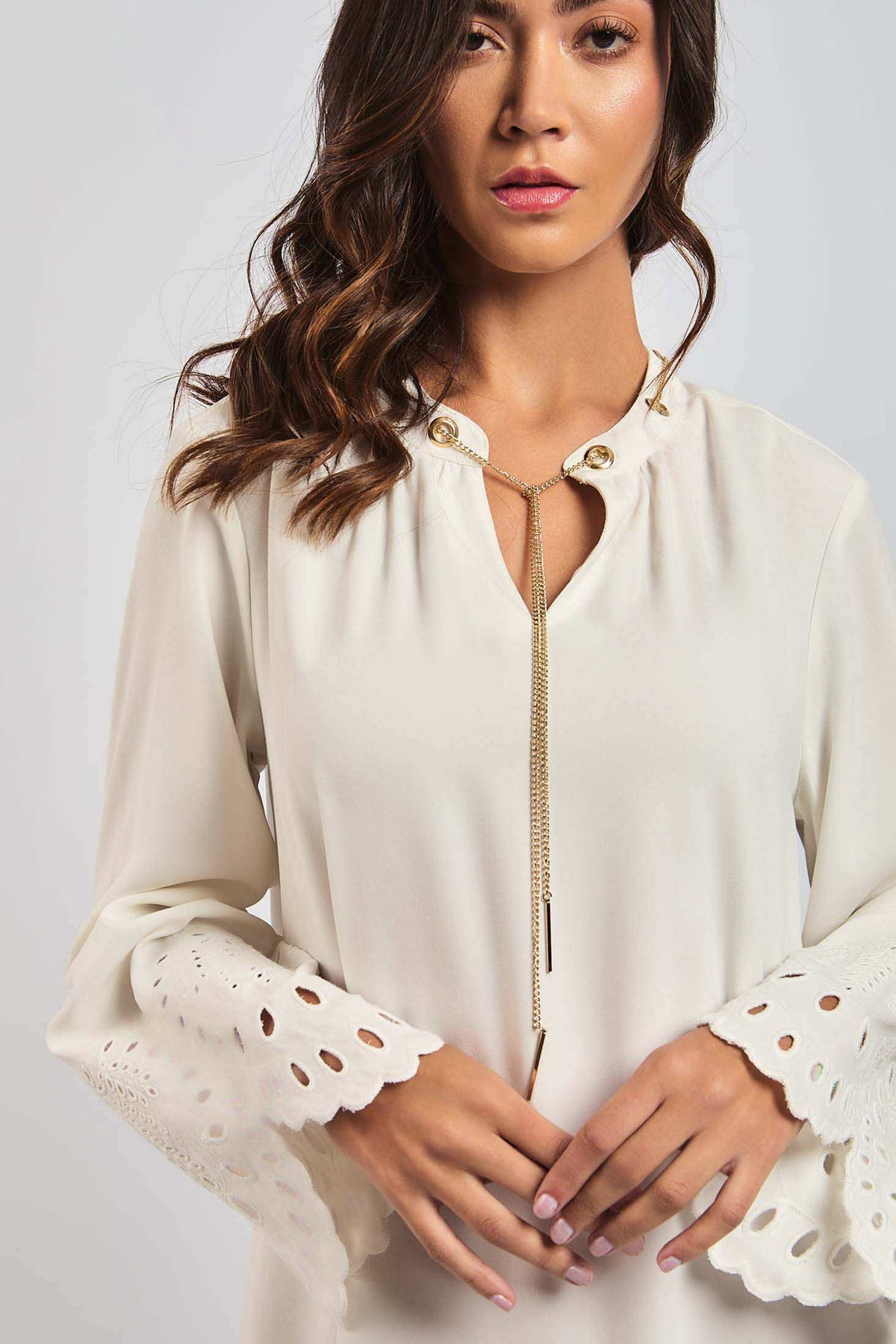 Woman wearing a cream blouse with eyelet lace bell sleeves and gold necklace