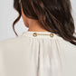 Back view of a woman wearing a cream blouse with gold chain detail on the collar