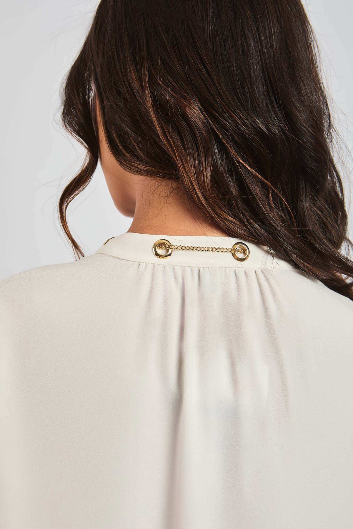 Back view of a woman wearing a cream blouse with gold chain detail on the collar