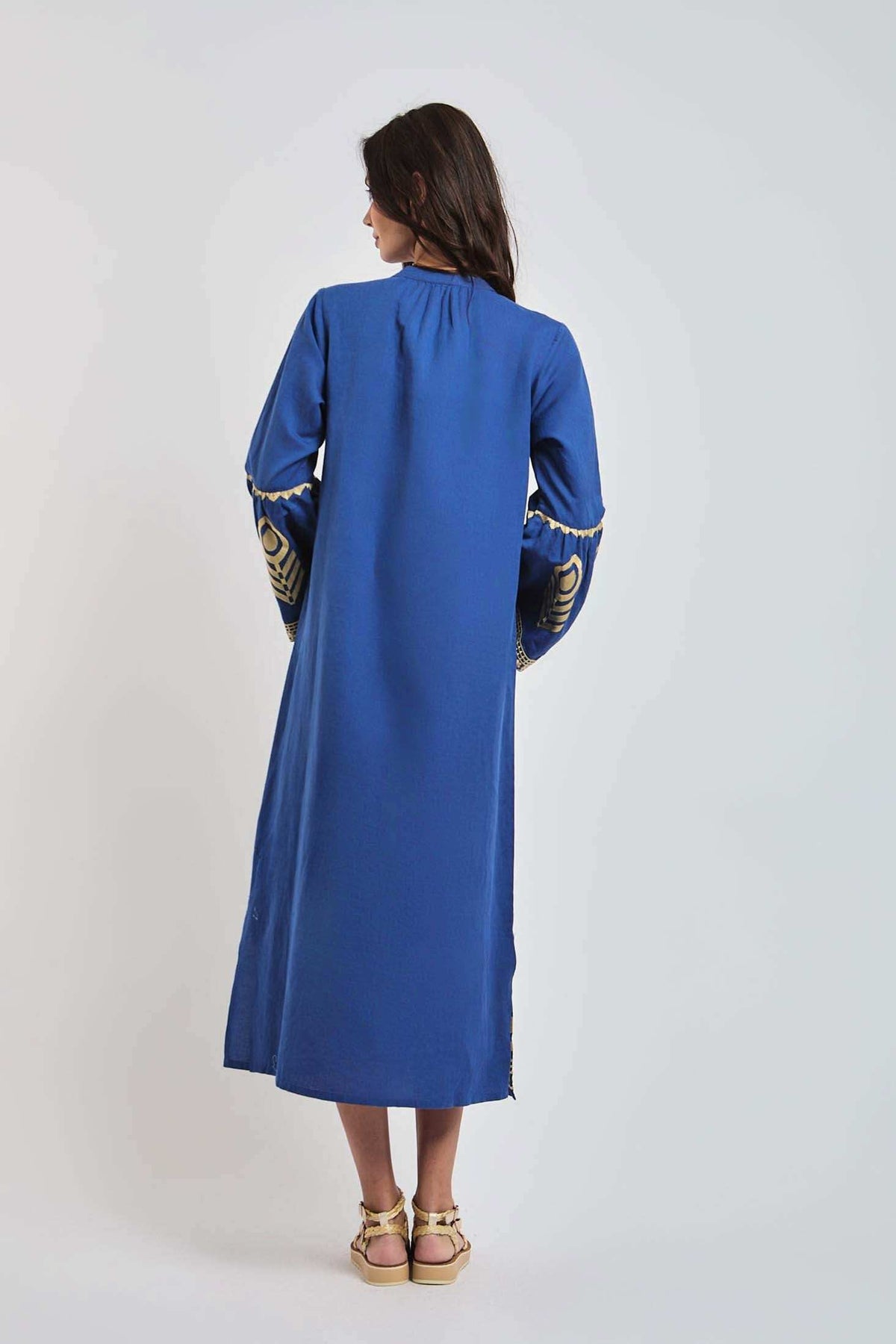 Woman wearing a long blue dress with gold embroidery details, back view