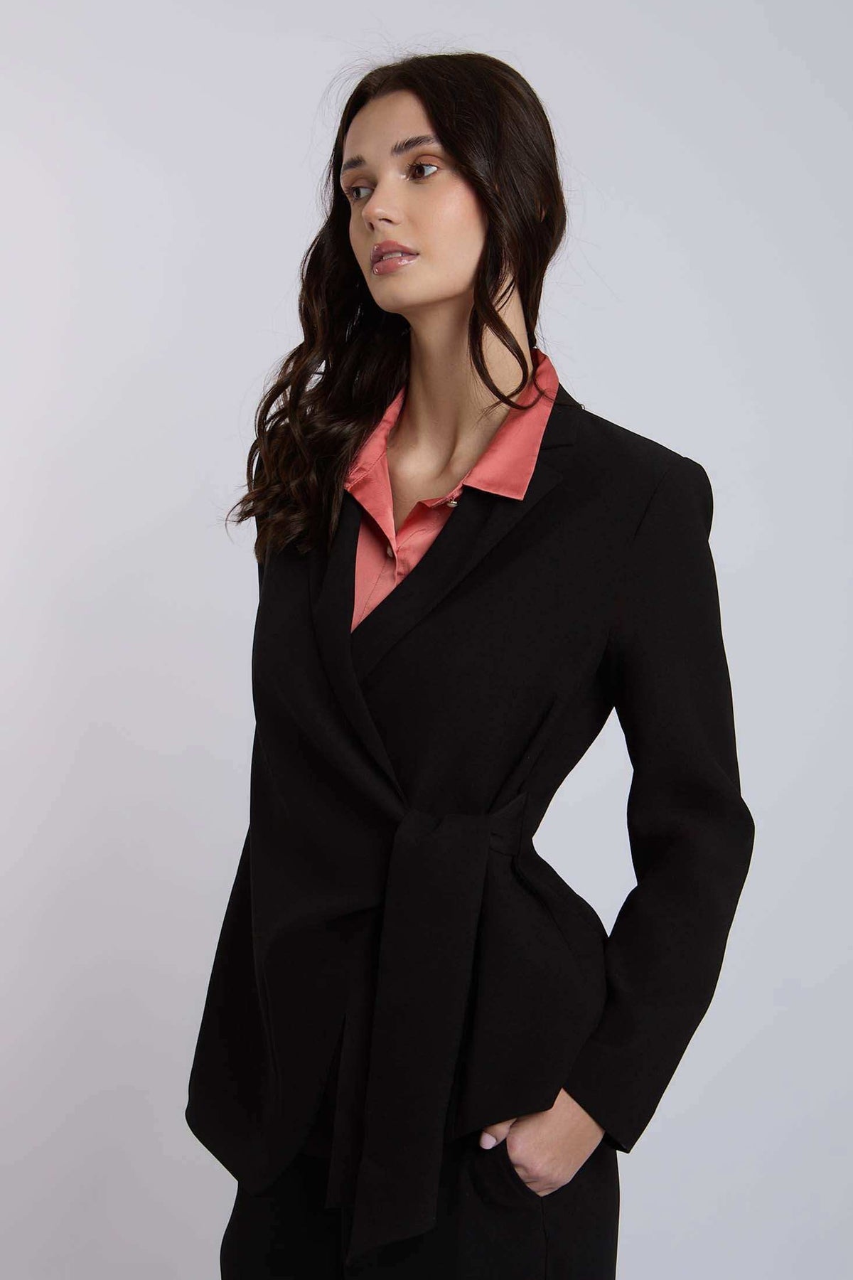 Woman wearing a black tailored blazer with tie waist over a pink collared blouse