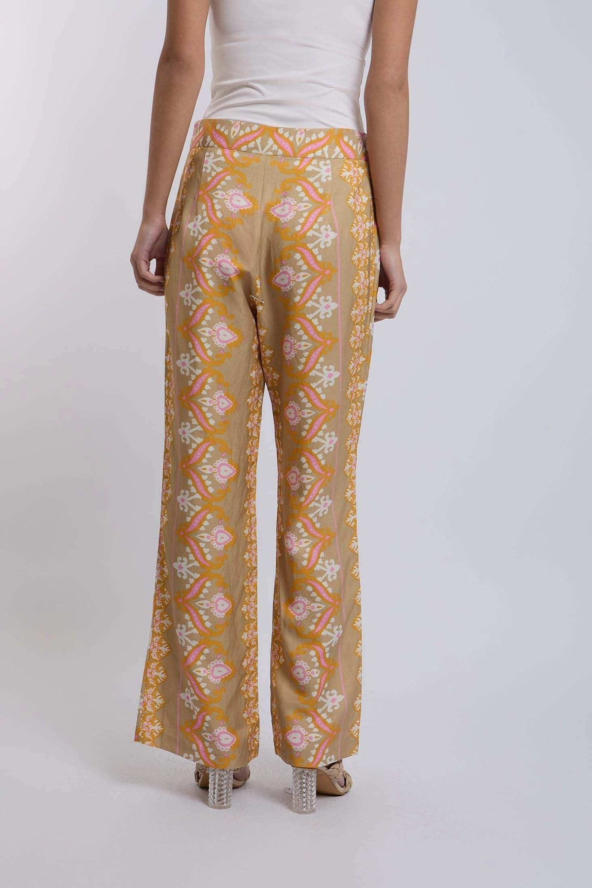 Women's patterned wide-leg pants in tan with pink and orange floral motifs, back view