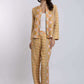 Woman wearing a beige patterned pantsuit with a white top, standing against a plain background