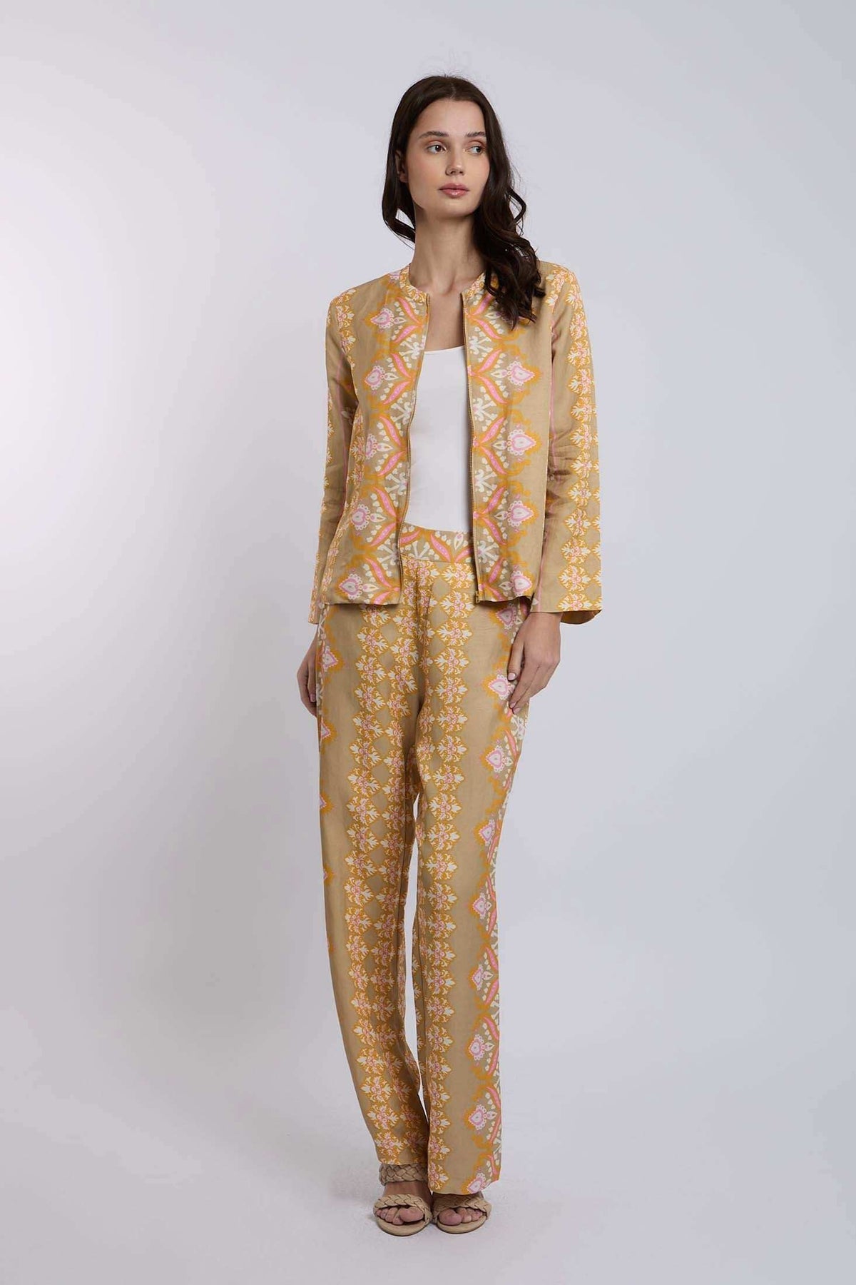 Woman wearing a beige patterned pantsuit with a white top, standing against a plain background