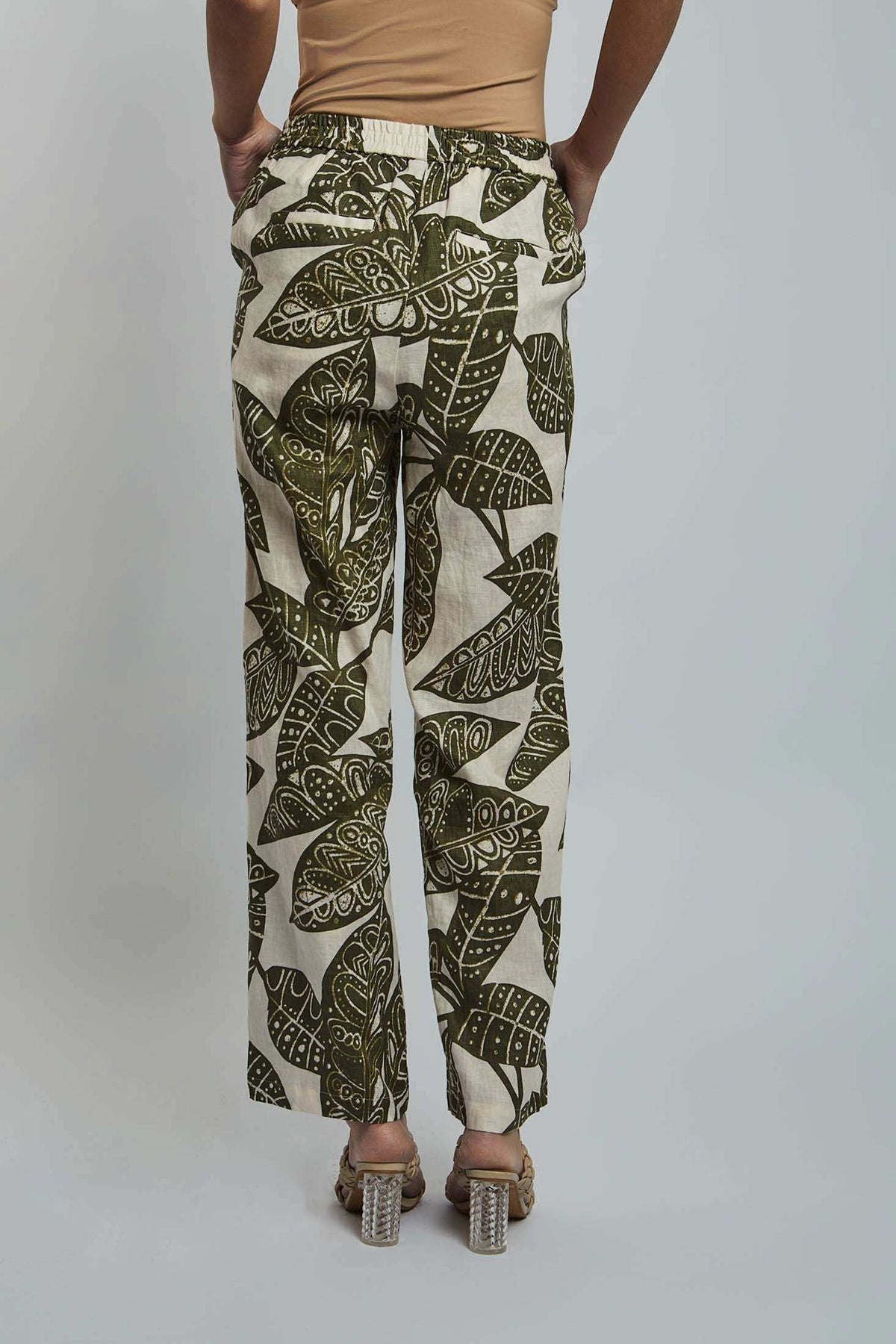 Woman wearing beige top and green leaf print wide leg pants, back view