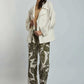 Woman wearing cream oversized jacket, beige top, and patterned leaf print trousers