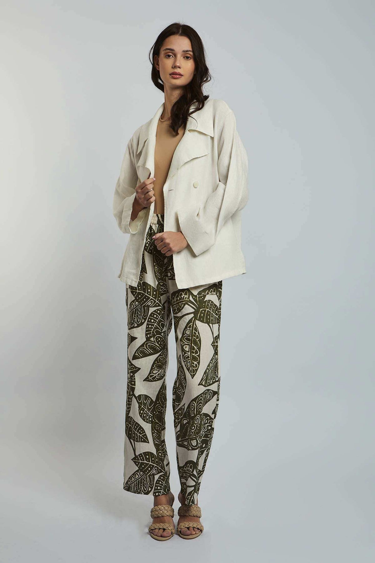 Woman wearing cream oversized jacket, beige top, and patterned leaf print trousers