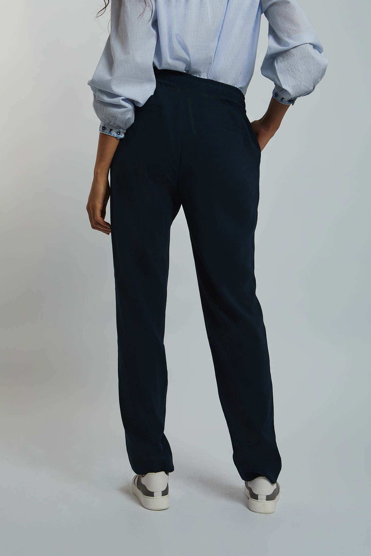 Woman wearing relaxed black pants and a light blue blouse, back view, casual fashion