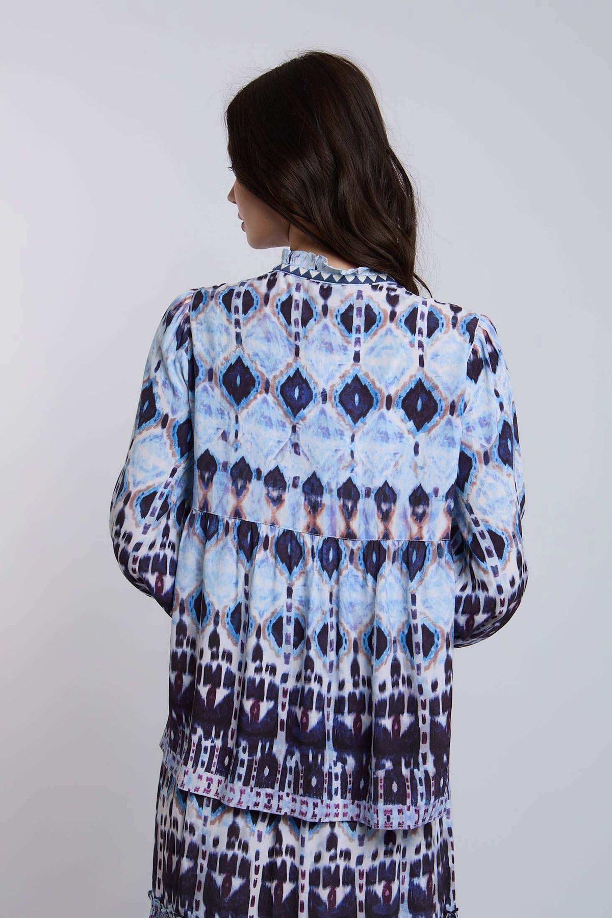 Woman in long sleeve blue and black patterned blouse and skirt, back view, casual style